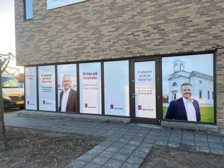 Facade med vinduesfolie fra SparNord, der viser to personer og teksten 'Vi tror på Hørsholm'.