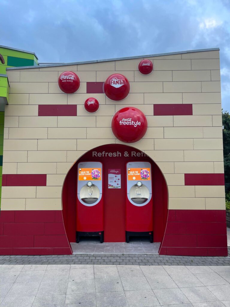 Coca-Cola Freestyle drikkeautomat med forskellige sodavandsmuligheder i en rød og beige væg.