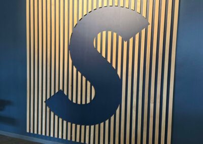 Blå væg med trælameller og et stort, stiliseret bogstav S i midten.