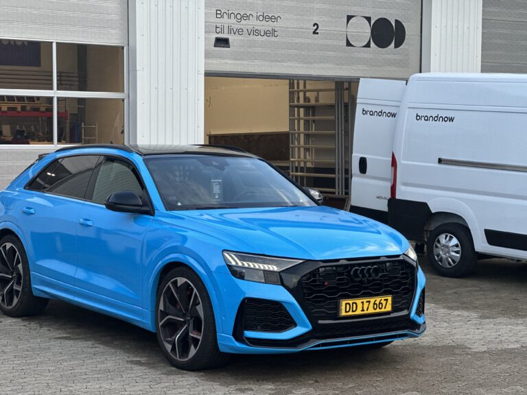 Blå Audi RSQ8 parkeret foran Brandnow's kontor med en hvid varevogn i baggrunden.