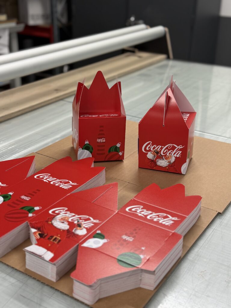 Røde juleæsker fra Coca Cola med julemotiver og logo.