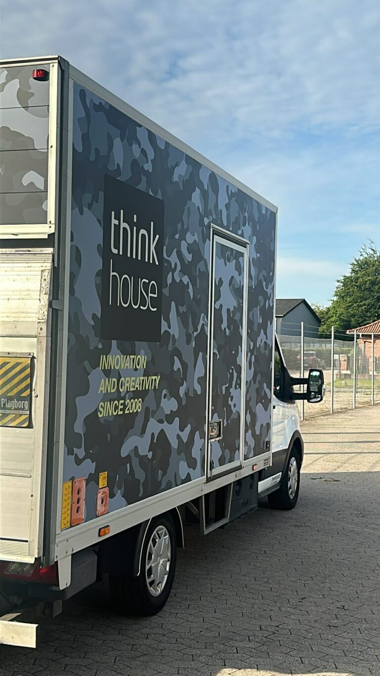 Lastbil med camouflage design og logo fra Thinkhouse, der angiver innovation og kreativitet siden 2008.