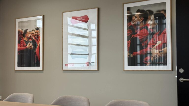 Hilti Danmark pryder væggen med tre indrammede plakater, hvor medarbejdere i rødt tøj og et Lead 2030-grafikmotiv ses i et mødelokale.